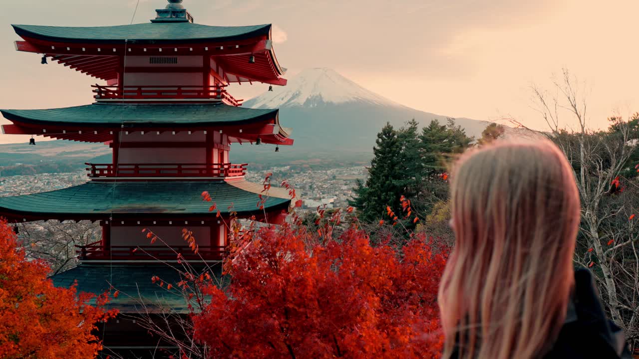 una captura cautivadora de una mujer capturando la icónica pagoda chureito al atardecer, enmarcada por las vívidas hojas rojas del otoño con el monte fuji en el fondo.