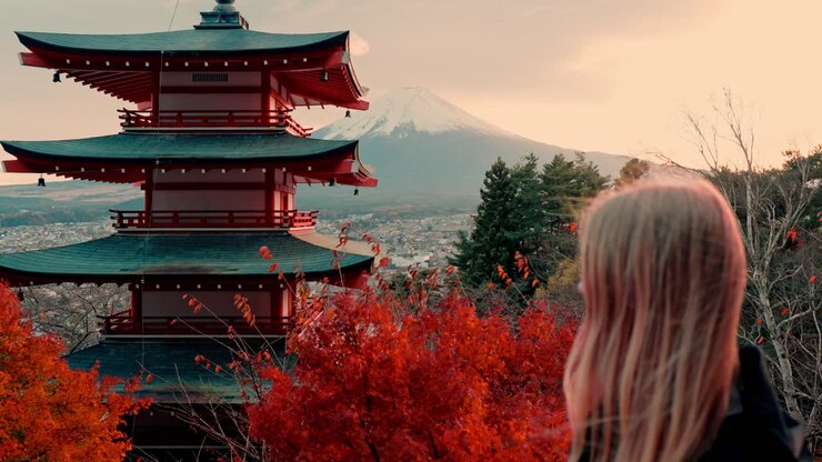 A captivating shot of a woman capturing the iconic Chureito Pagoda at sunset, framed by the vivid red leaves of autumn with Mount Fuji in the background.
