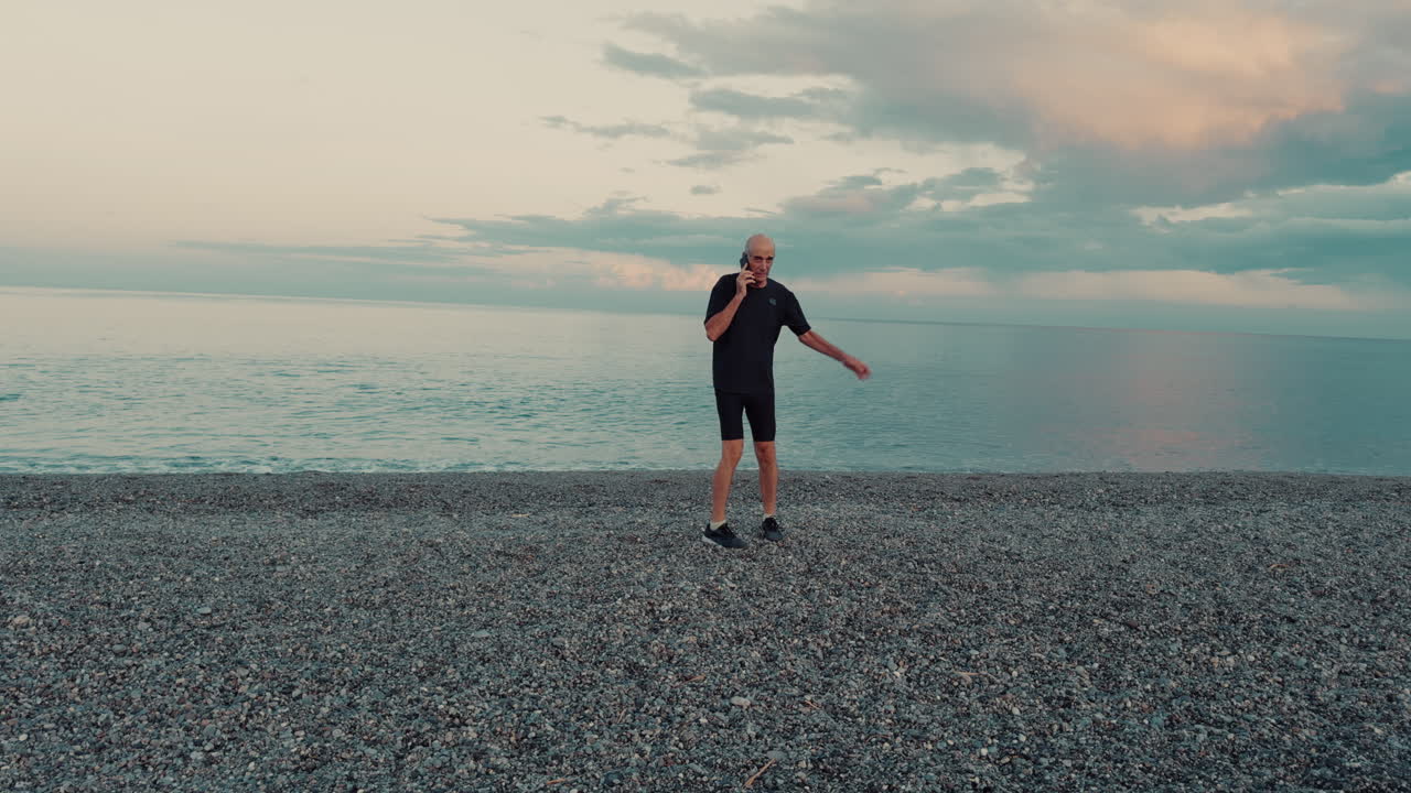 Elderly man walking on the beach near the sea talking on the phone seriously