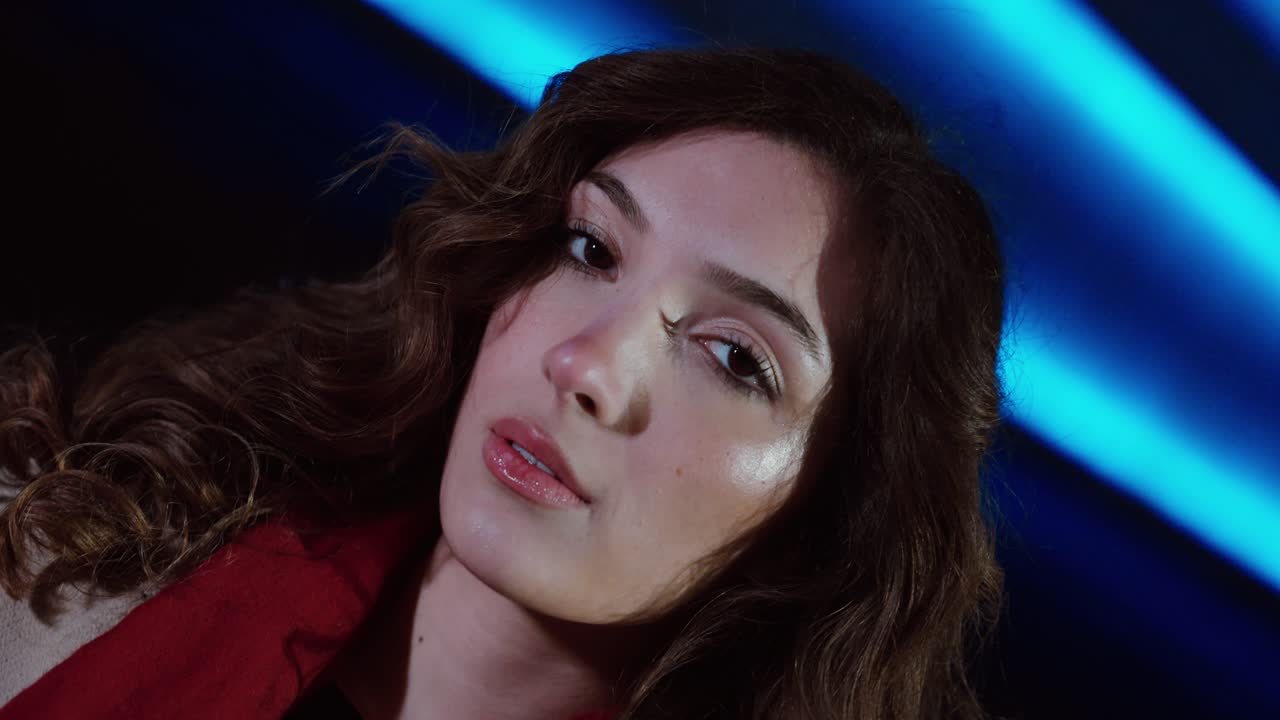 Ripresa FPV con inclinazione del gimbal di una bella donna con capelli ricci sotto luci al neon blu di notte, che crea un dinamico ritratto di moda cinematografico. Concetto per l'estetica moderna della vita notturna