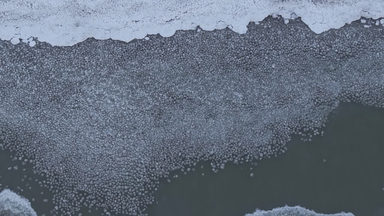 A partially frozen lake with ice patterns, aerial view