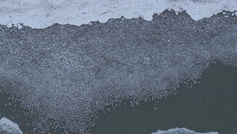 a partially frozen lake with ice patterns, aerial view