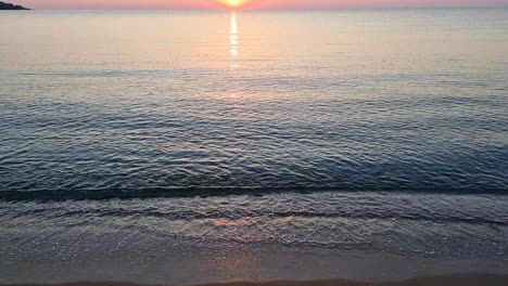 superficie de agua tranquila y olas de mar salpicando en la playa de arena al amanecer