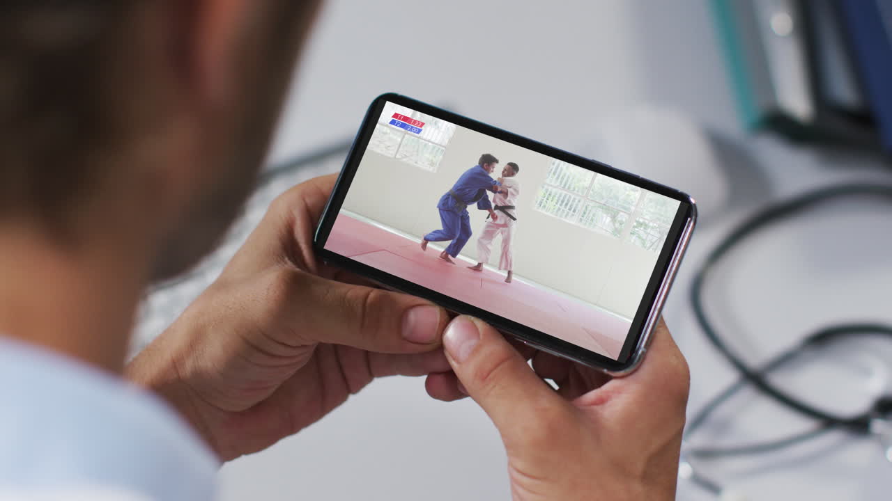 composición de un médico masculino viendo un partido de judo en un teléfono inteligente