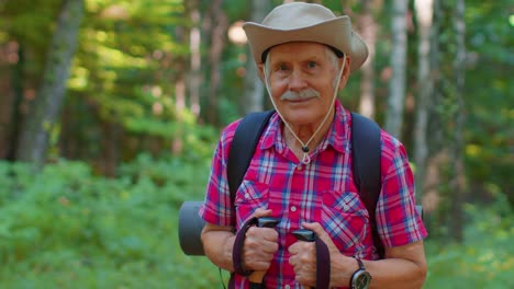 Senior-old-Caucasian-tourist-hiker-grandfather-training-Nordic-walking-with-trekking-poles-in-forest