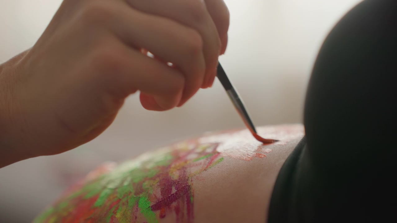Primo piano di una mano che dipinge un disegno colorato sulla pancia incinta