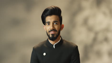 young cheerful indian man with beard and in black jacket looking at camera and smiling cheerfully