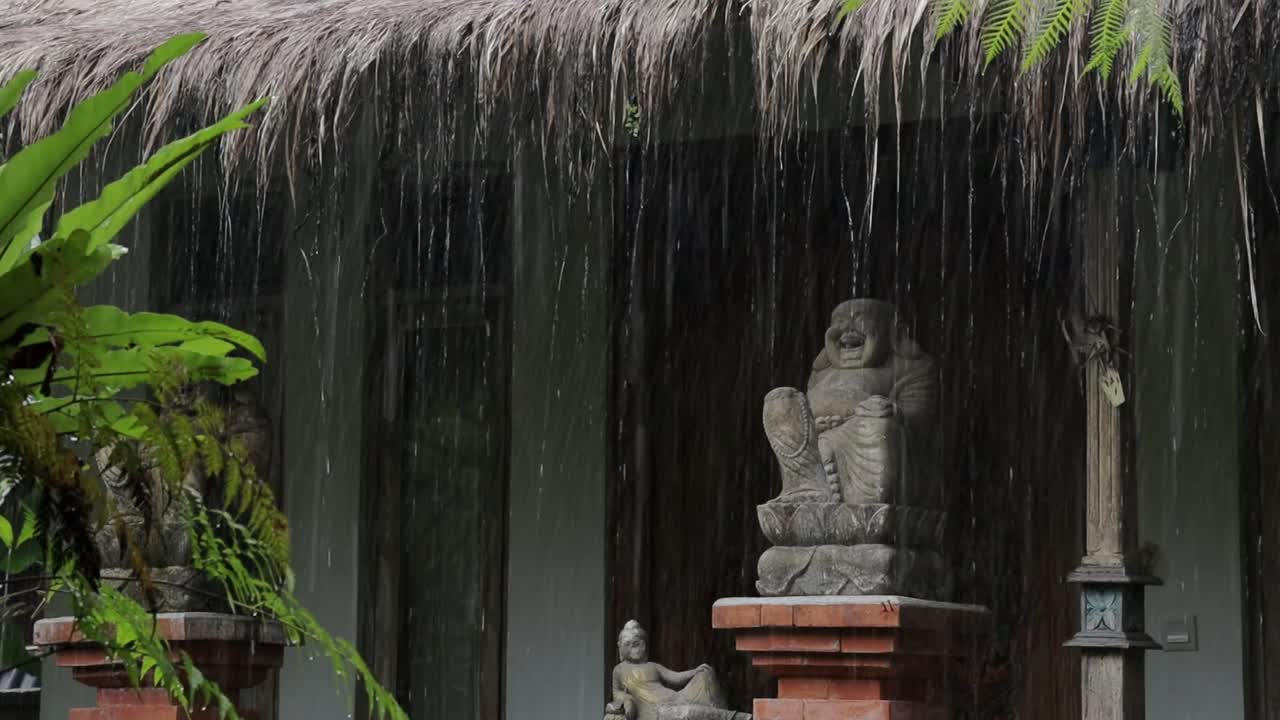 gotas de lluvia monzónicas en la casa tropical tradicional de bali, estatua de buda sonriente