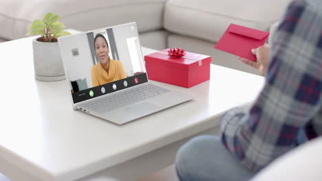 Caucasian-man-holding-red-envelope-using-laptop-with-african-american-woman-on-screen