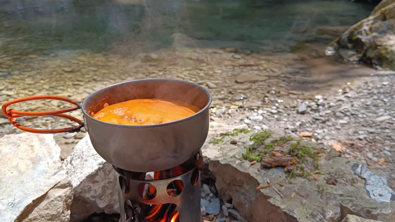 la sopa de tomate está hirviendo en una hoguera junto al río y la cascada