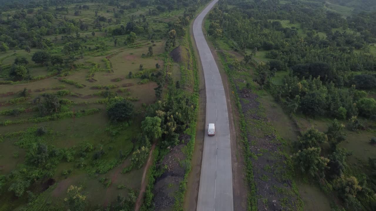 Drone following a caravan traveling on a rural Indian road of good quality with the surroundings of lush green forest land