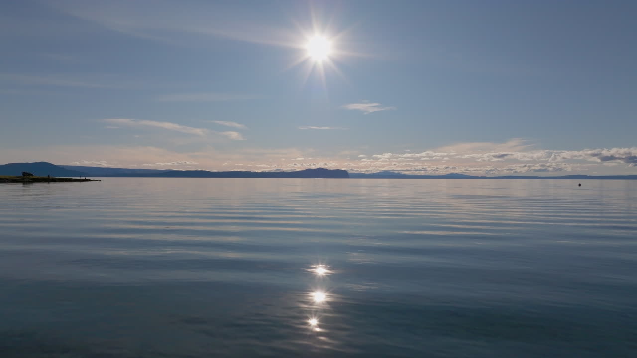 Flying low over Lake Taupo with bright sunlight reflecting on the calm water, New Zealand.