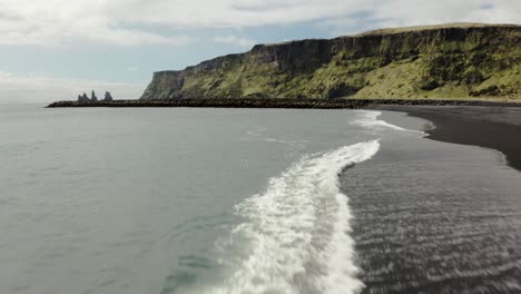 aerial shot of black sand shore over the waves moving forward