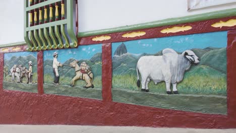 colorful wall mural in guatapé depicting traditional rural life with animals and mountains.