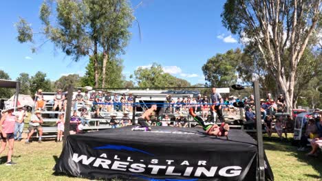 wrestlers compete in an outdoor ring before audience