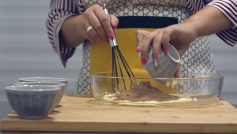 leiria, portugal - woman puts chocolate powder to a mixing bowl in slow motion before whisking - closeup shot