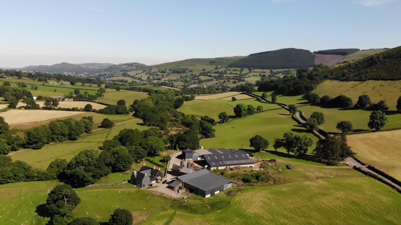 Aerial shot of a farm in Wales with the beautiful countryside in the background with hills, fields, and trees