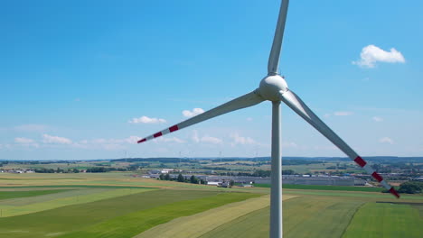 Rotating-wind-turbine-agains-blue-sky-in-green-farm-landscape,-aerial