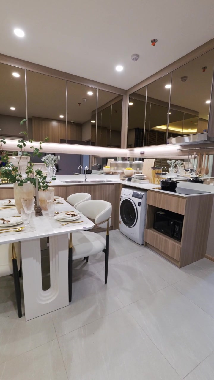 Tour pelo interior de um condomínio de luxo moderno mostrando uma mesa de jantar elegante com cadeiras, cozinha aberta com armários espelhados e porta que leva ao quarto em Chiang Mai, Tailândia