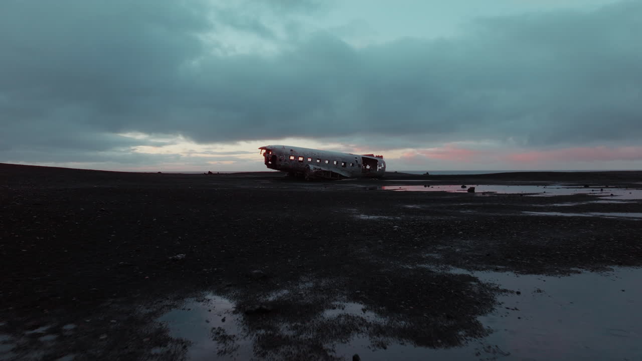 아이슬란드 솔헤이마산두르의 검은 모래 해변에서 버려진 dc 비행기의 무인기 영상, 어두운, 영화적인 톤으로 구름이 많은 일출 아래에서 포착되었습니다.