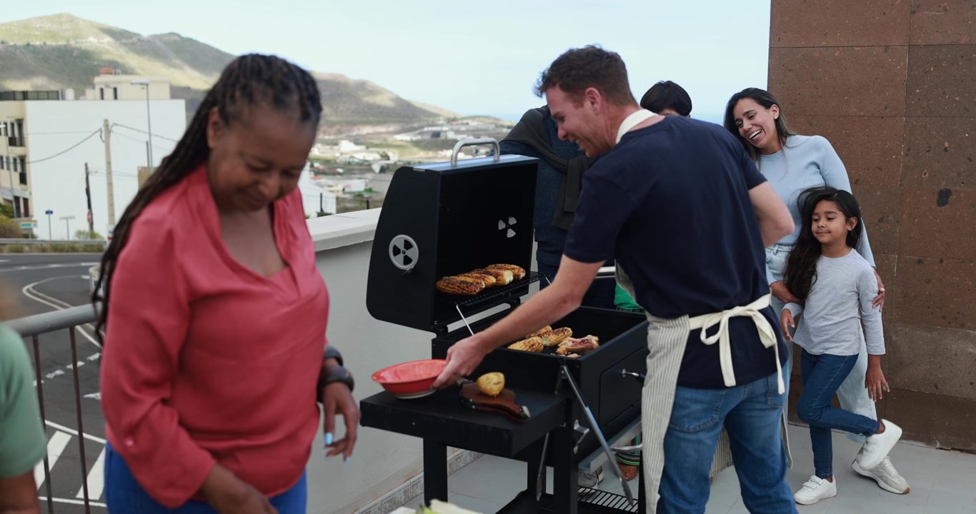 Famiglia e amici multietnici felici che fanno una grigliata su una terrazza panoramica