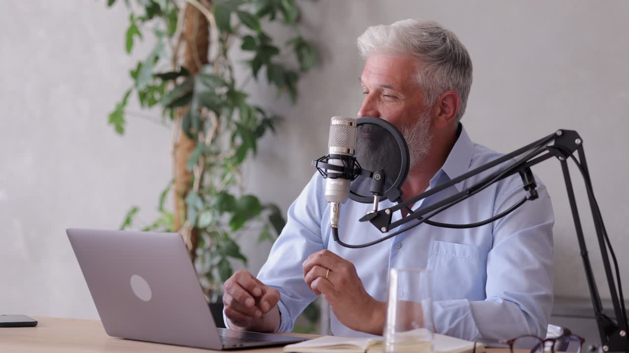 En mand optager en podcast eller et interview med en mikrofon i et lydstudie. En senior lydtekniker eller radiovært. En voksen gråhåret mand skaber lydindhold.