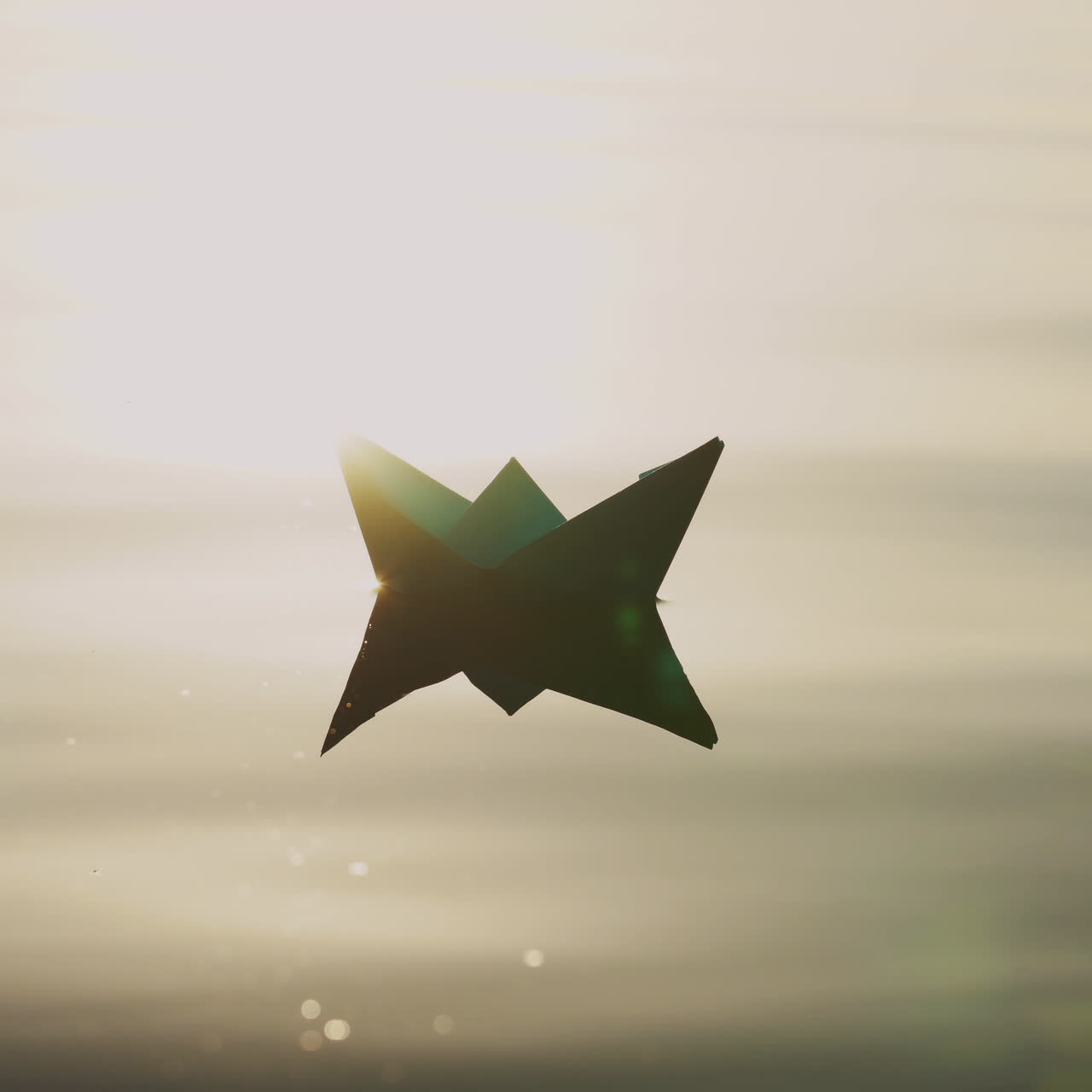 Paper boat floats alone with its reflection on the wavy water in the river at sunset. Beautiful rays of the evening sun falling on origami ship.Close-up