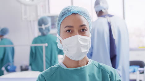 video portrait of biracial female surgeon in face mask in operating theatre, with copy space