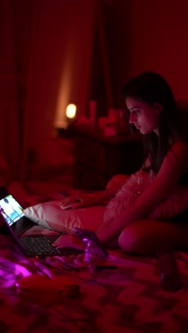 young woman watching a video on a laptop in a bedroom at night.