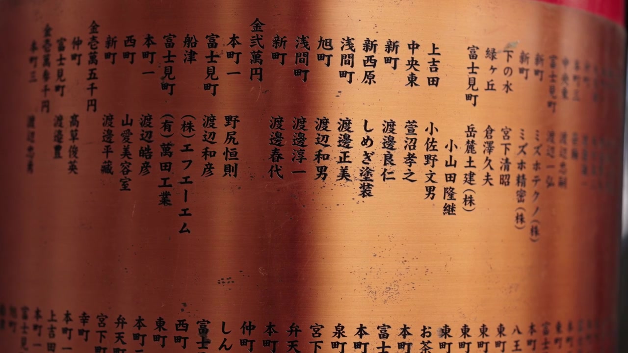 Colonna curva in legno laccato di un santuario con nomi di donatori in kanji incisi verticalmente sulla superficie, Giappone.