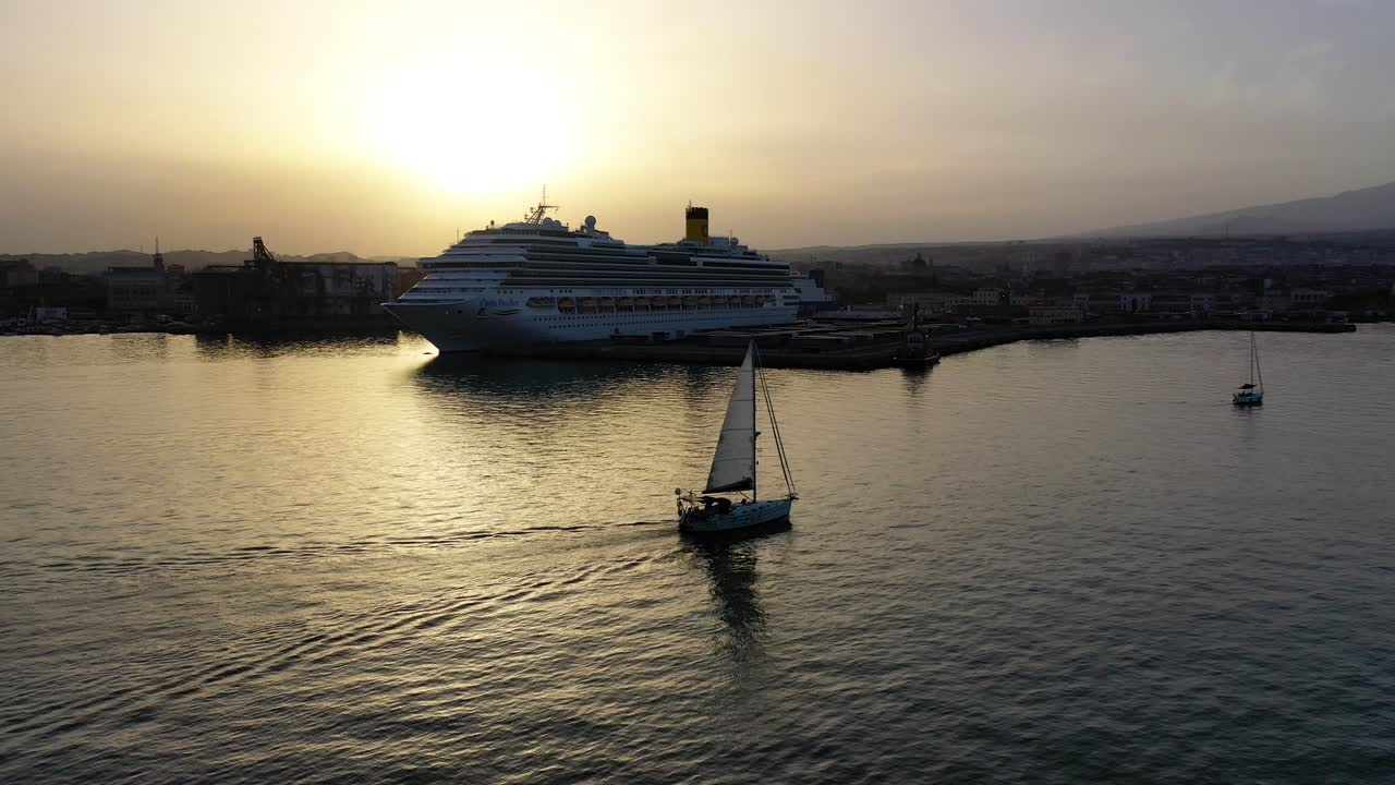pequeño velero navegando en el agua del océano al atardecer hora dorada del crepúsculo, gran barco de crucero en el fondo - vista aérea