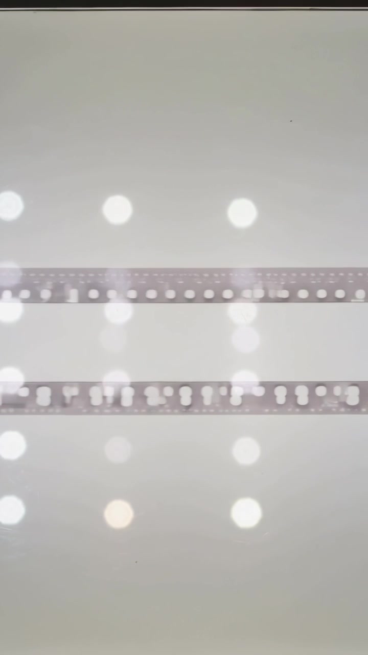 Vertical video: Flickering lights shifting bokeh over two film strips on wall, dark band appearing