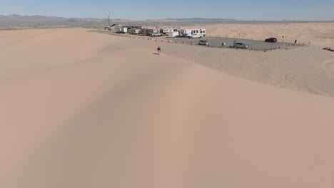 Approaching-Sand-Dune-Camping-Spot-with-Drone,-Aerial-Shot-of-RV's-and-Trailers-Set-Up-by-Desert-Sand-Dune-Landscape