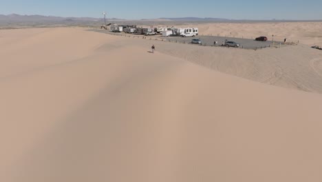 approaching sand dune camping spot with drone, aerial shot of rv's and trailers set up by desert sand dune landscape