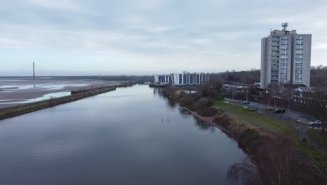 Aerial-view-flying-old-British-town-regeneration-waterfront-apartments-block-along-waterway-channel-pull-away-slow