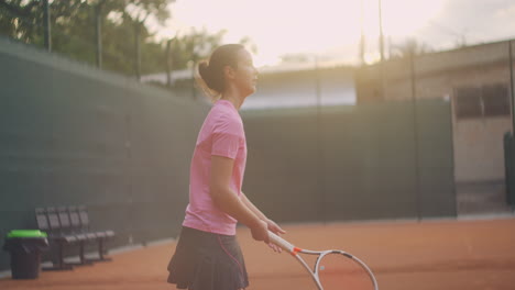 A-tired-brunette-female-tennis-player-walks-along-the-tennis-court-recuperating-and-concentrating.-Break-in-a-tennis-match.-Tennis-player-after-the-match-on-the-map-at-sunset-in-slow-motion.