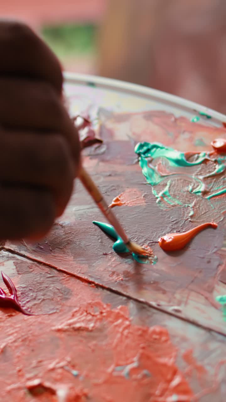 Artist's Hand Mixing Vibrant Paint Colors on a Palette