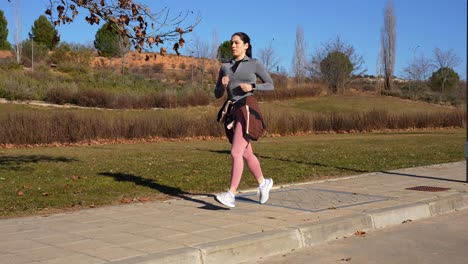fit woman jogging outdoors in a sunny park, ponytail bouncing, focused and active