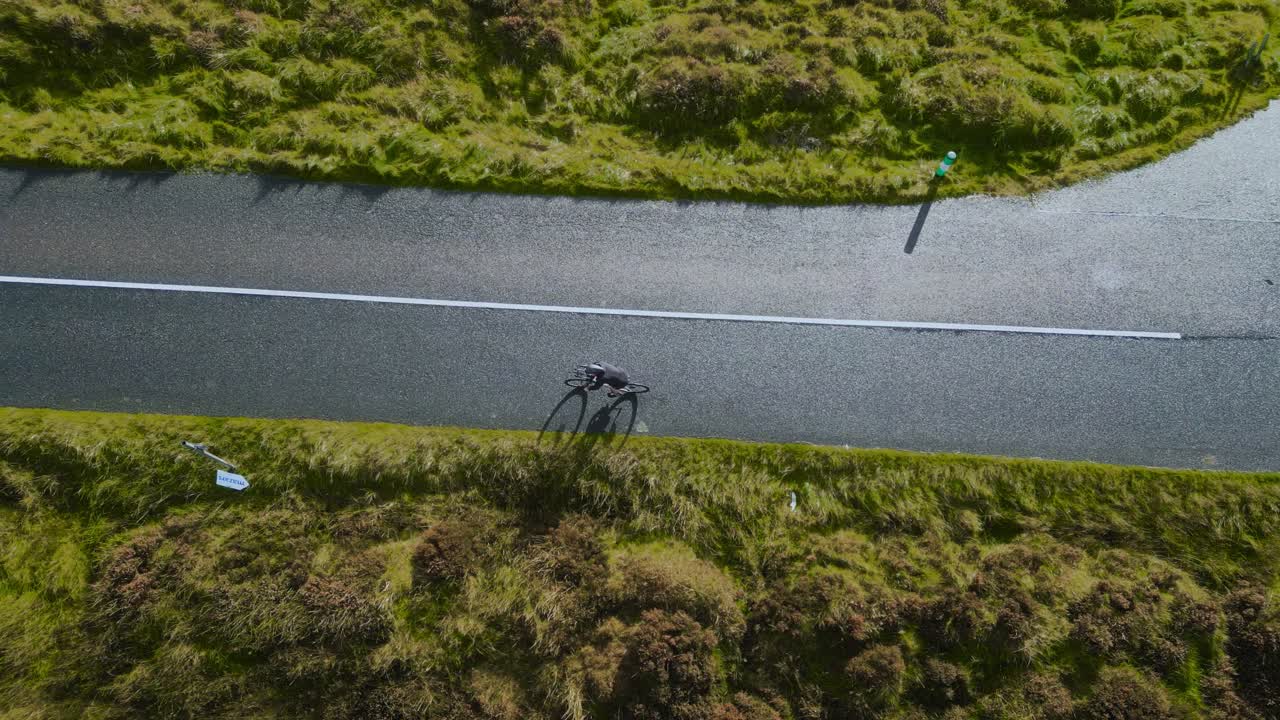 Top view a lone cyclist on a winding road in the Dublin Mountains, featuring a "STOP" road marking and rugged Irish hills