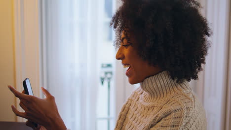 Positive-girl-using-smartphone-at-home.-Curly-smiling-lady-trying-mobile-phone