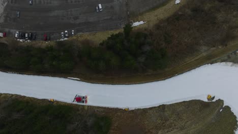 a red snow plow in snowy saalbach-hinterglemm , ski resort, dolly left, birdseye view, overcast day, aerial view