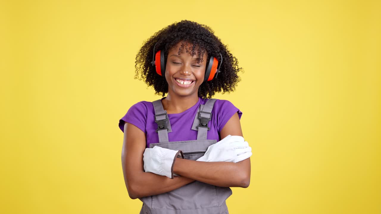 Donna sorridente in tuta da lavoro e cuffie antirumore su sfondo giallo.