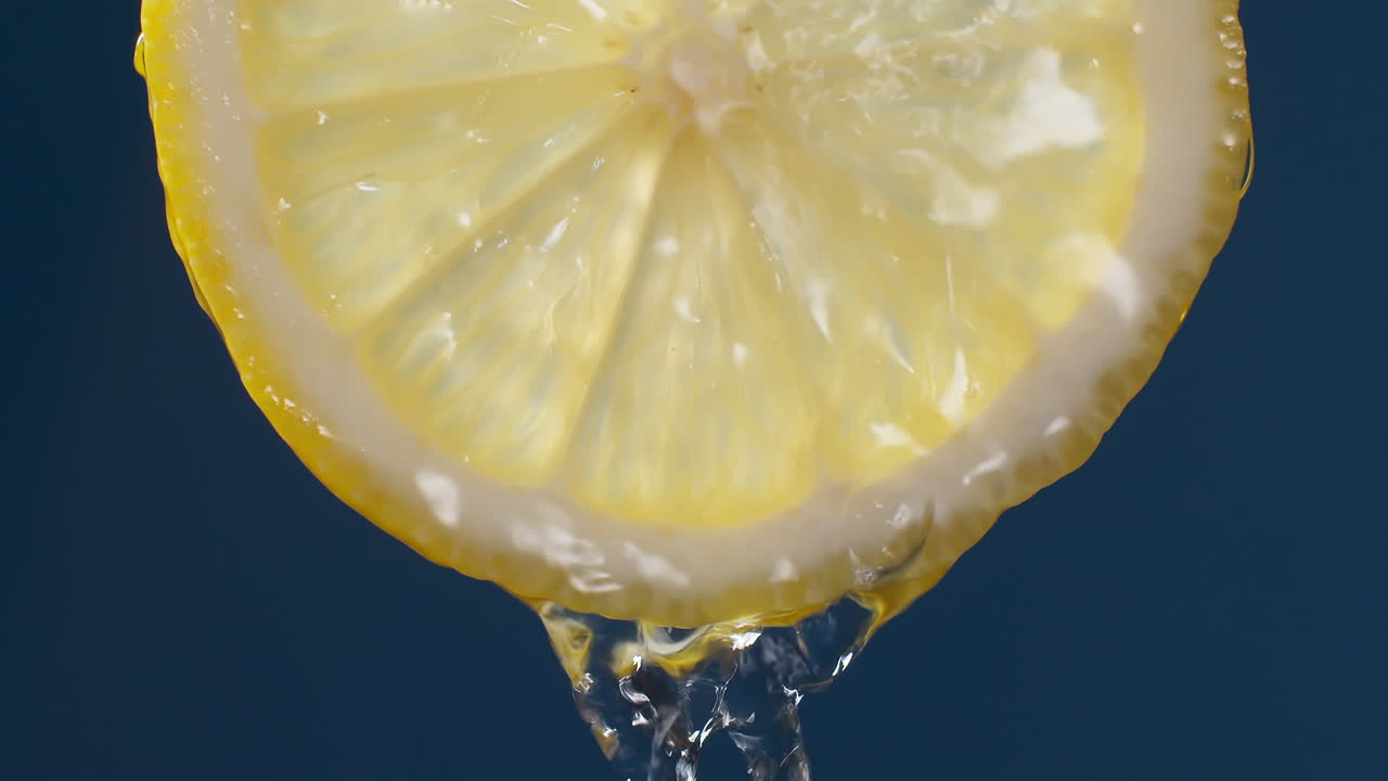 파란색 검정색 배경에 있는 레몬 슬라이스에서 흐르는 물의 슬로우 모션 매크로 샷