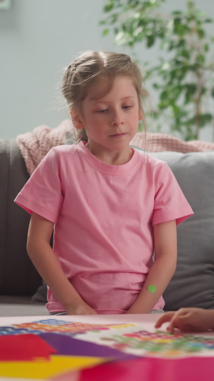 Little boy looks at colorful dot sticker elder sister sits nearby watching brother on sofa at home slow motion. Development of children creativity. Art work