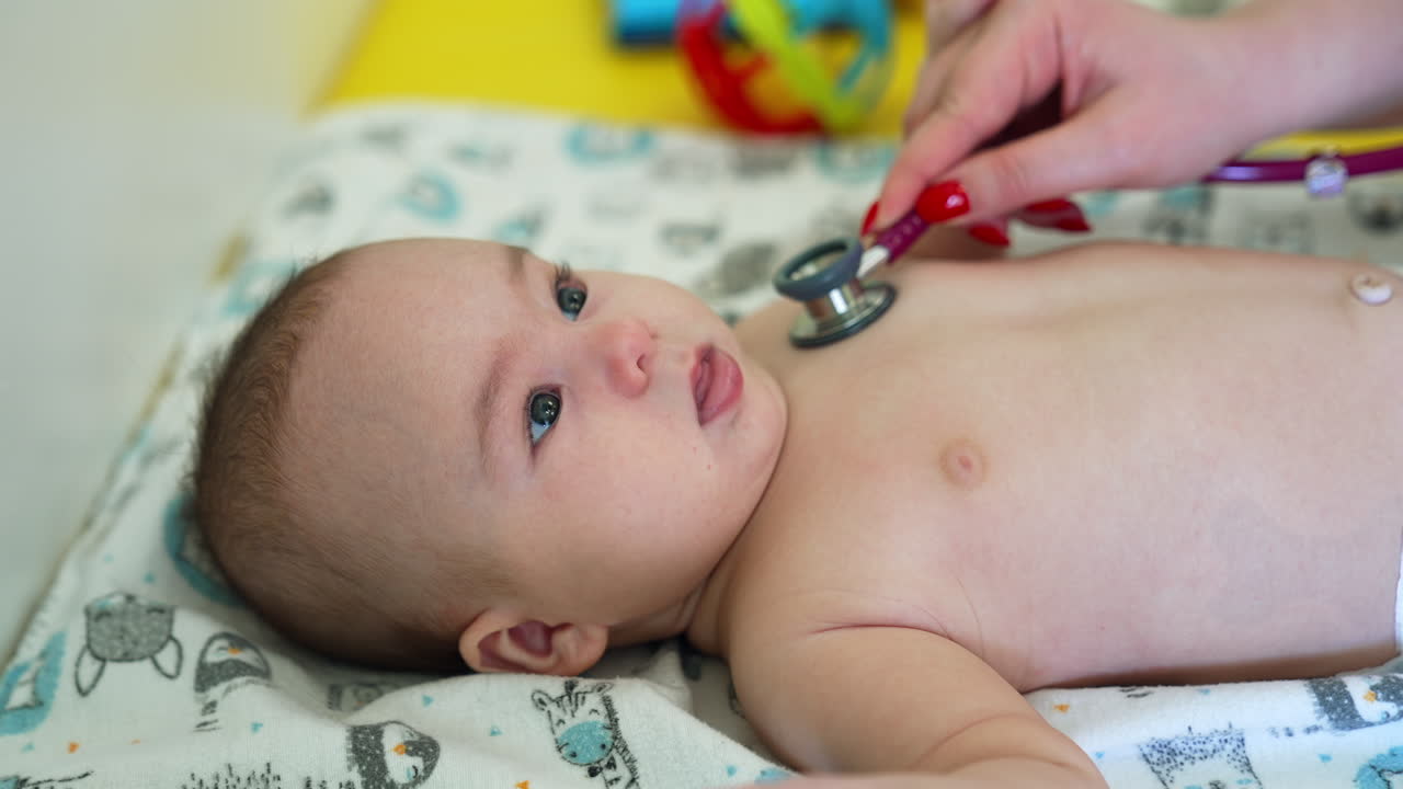 Doctor is putting stethoscope on baby's bare chest. Little kid is smiling sweetly and showing tongue to the doctor. Close up.