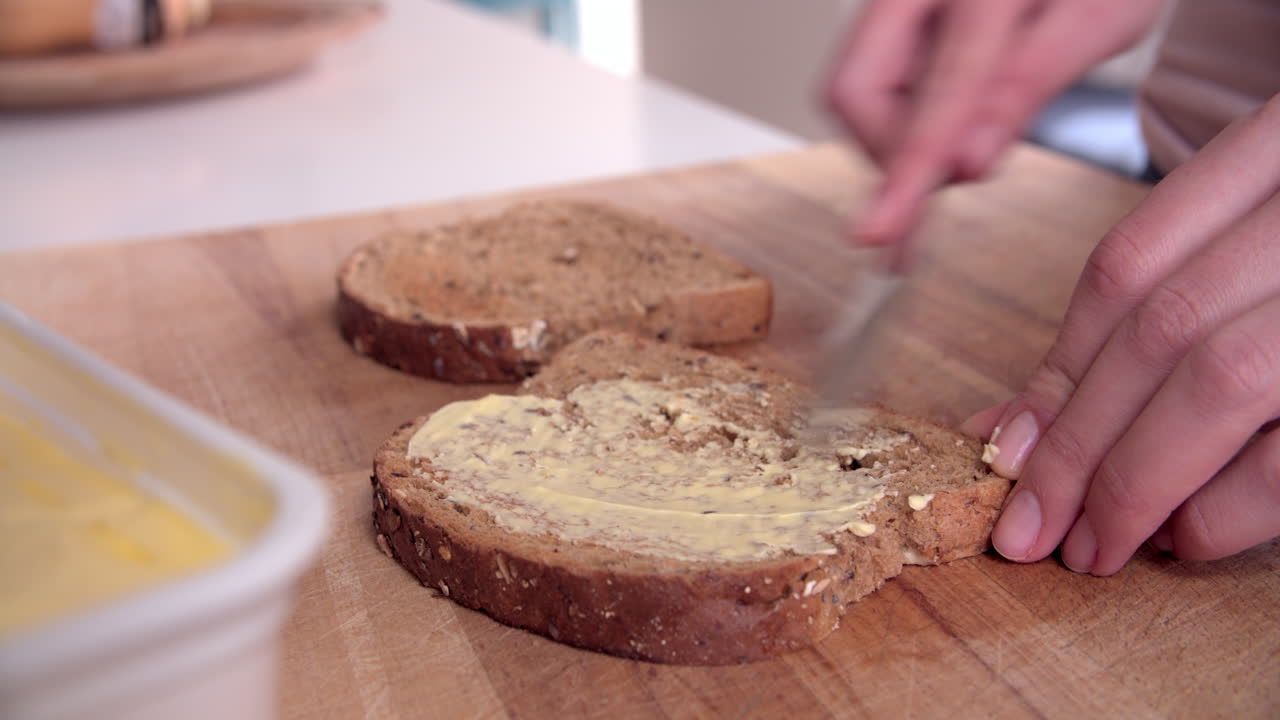 Person Spreading Butter Onto Slice Of Toast