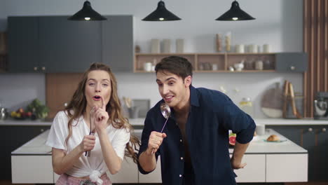 cheerful couple singing song in kitchenware at home kitchen. friends having fun