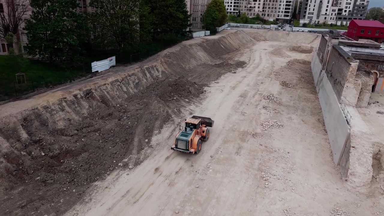 Wheel loader driving on dirt track in large excavation pit in an urban area. Aerial drone