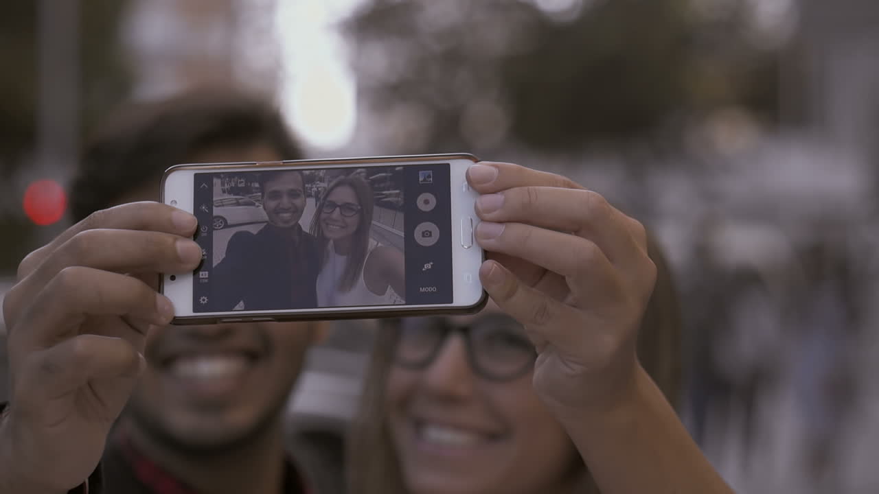 una joven pareja sonriente tomando una selfie con un teléfono inteligente