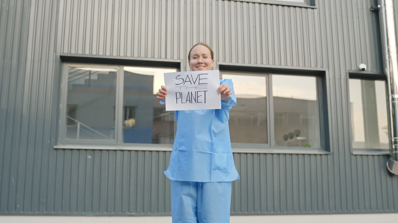Female Protester Holding a Message "Save the Planet" in Front of a Laboratory Building Wearing Blue Protective Outfit